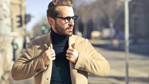 homme à lunettes portant un pull noir et une veste beige